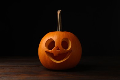 Photo of Scary jack o'lantern made of pumpkin on wooden table in darkness. Halloween traditional decor