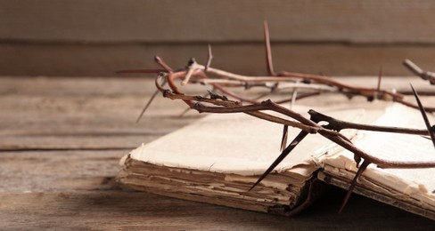 Photo of Crown of thorns and Bible on wooden table, closeup. Space for text