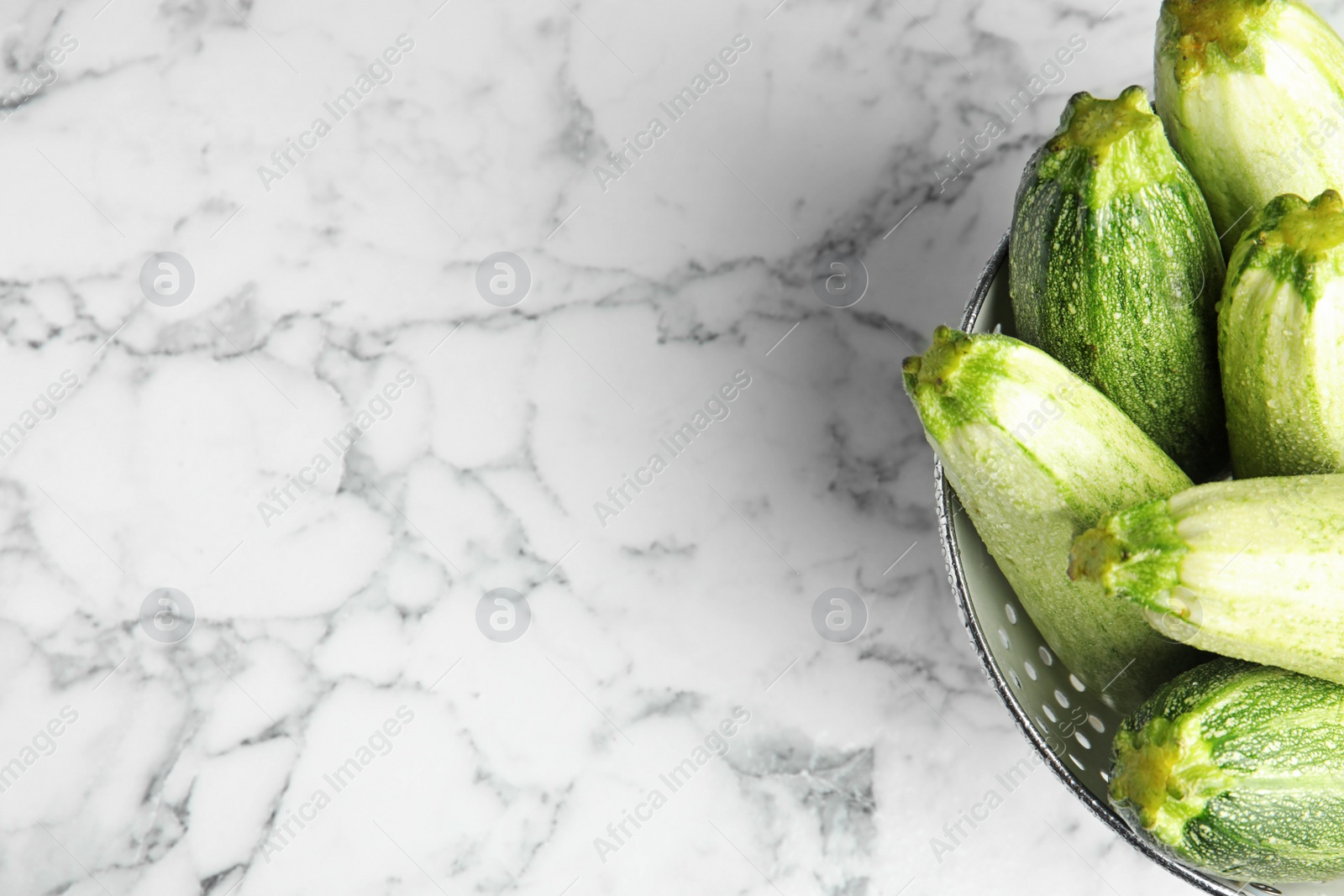 Photo of Colander with fresh ripe green zucchinis on marble table, top view. Space for text