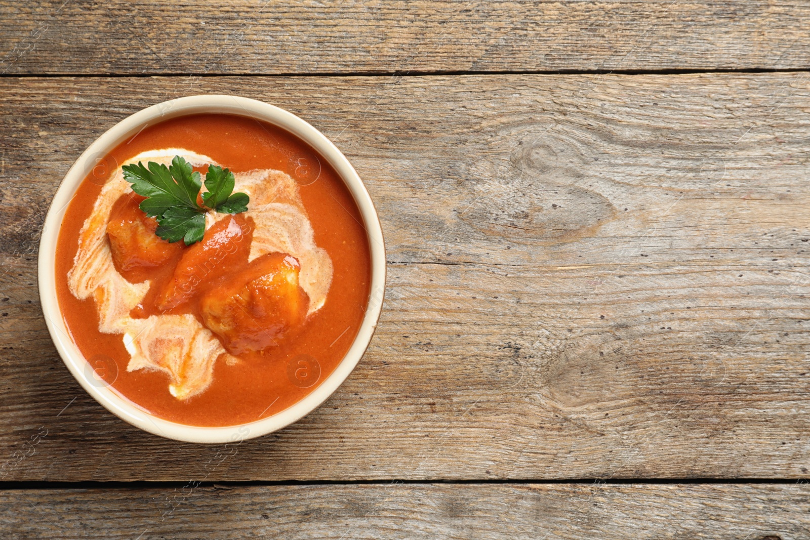 Photo of Bowl of delicious butter chicken on wooden background, top view with space for text. Traditional indian Murgh Makhani