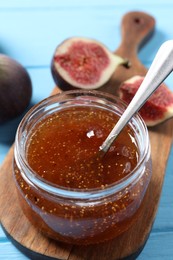 Jar of tasty sweet jam and fresh figs on light blue wooden table, closeup