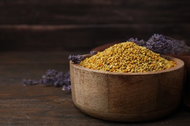 Fresh bee pollen granules in bowl and lavender on wooden table, closeup. Space for text