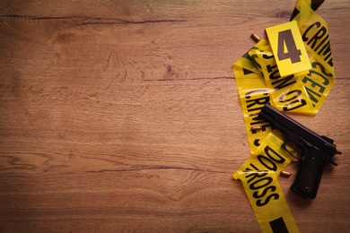 Photo of Flat lay with yellow tape, crime scene marker and gun on wooden background. Space for text