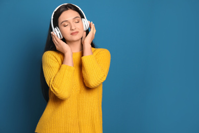 Young woman listening to audiobook on blue background. Space for text