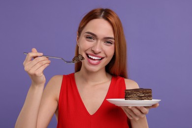 Young woman eating piece of tasty cake on purple background