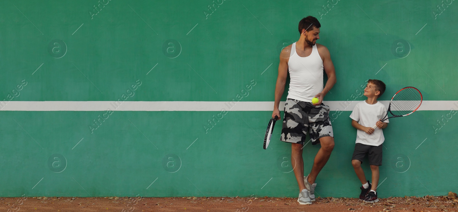 Image of Father with his son near green wall on tennis court. Banner design with space for text