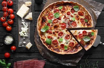 Cut delicious homemade quiche with prosciutto and ingredients on black wooden table, flat lay