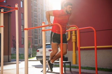 Photo of Man training on parallel bars at outdoor gym on sunny day