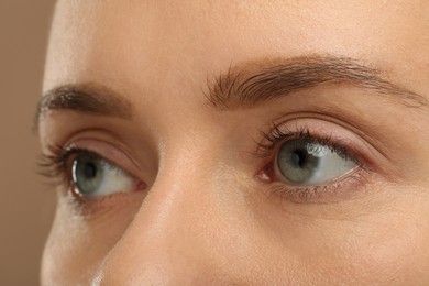 Photo of Woman with beautiful natural eyelashes on light brown background, closeup