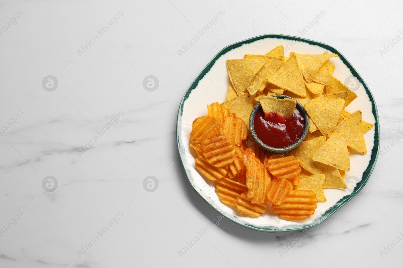 Photo of Plate with tasty ketchup, ridged and tortilla chips on marble table, top view. Space for text