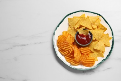 Plate with tasty ketchup, ridged and tortilla chips on marble table, top view. Space for text