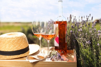 Photo of Bottle and glasses of wine on wooden table in lavender field
