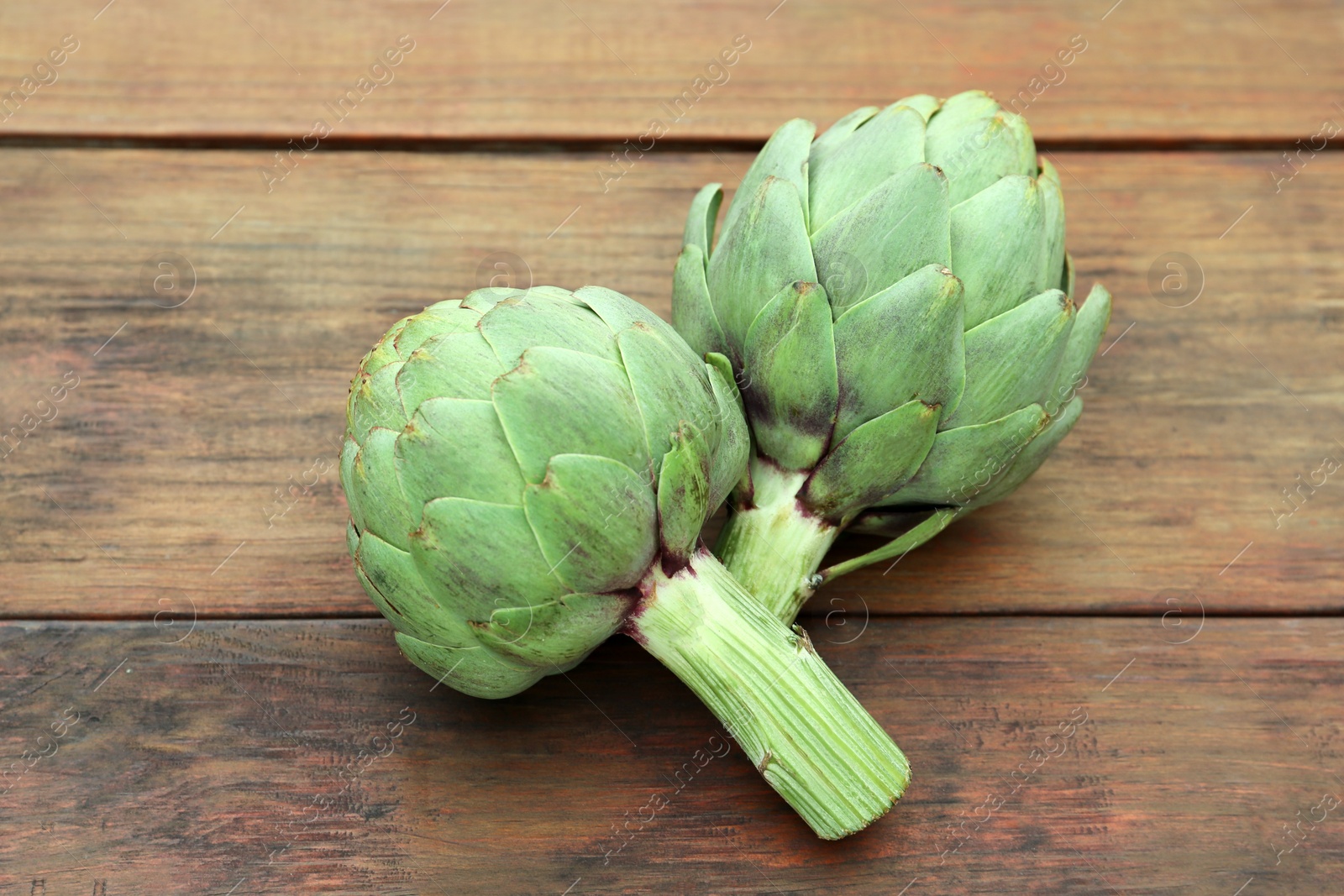 Photo of Fresh raw artichokes on wooden table, closeup