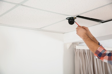 Electrician with screwdriver repairing CCTV camera indoors, closeup. Space for text