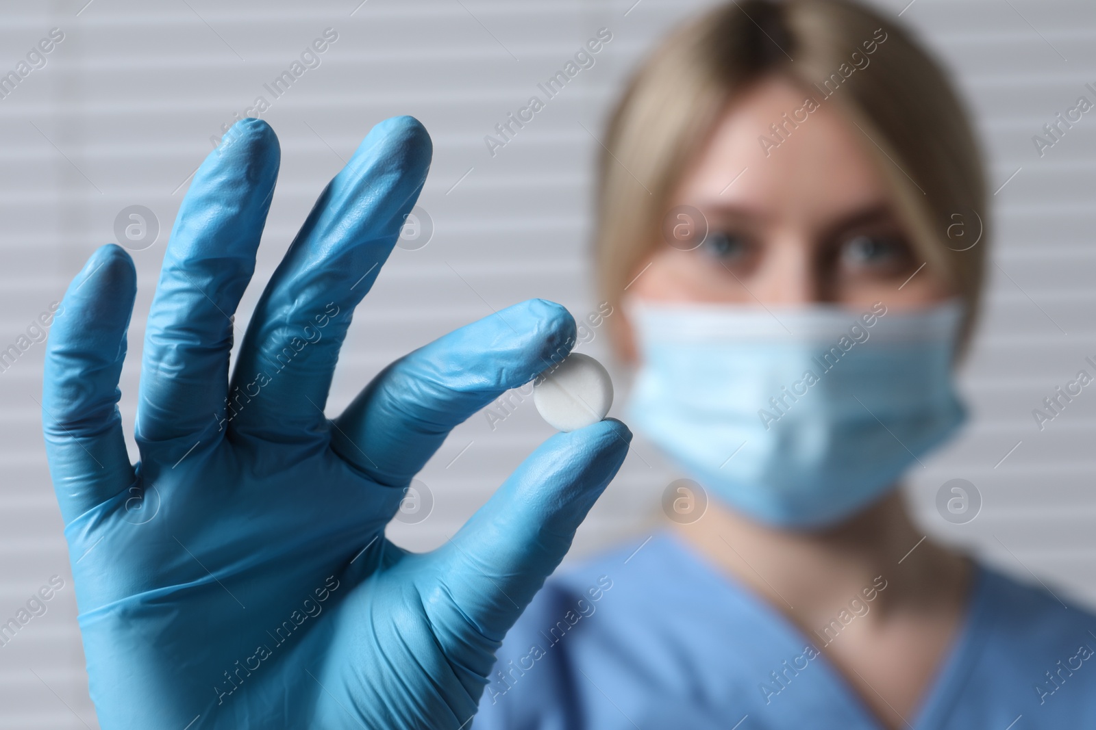 Photo of Doctor holding pill on light background, selective focus. Space for text