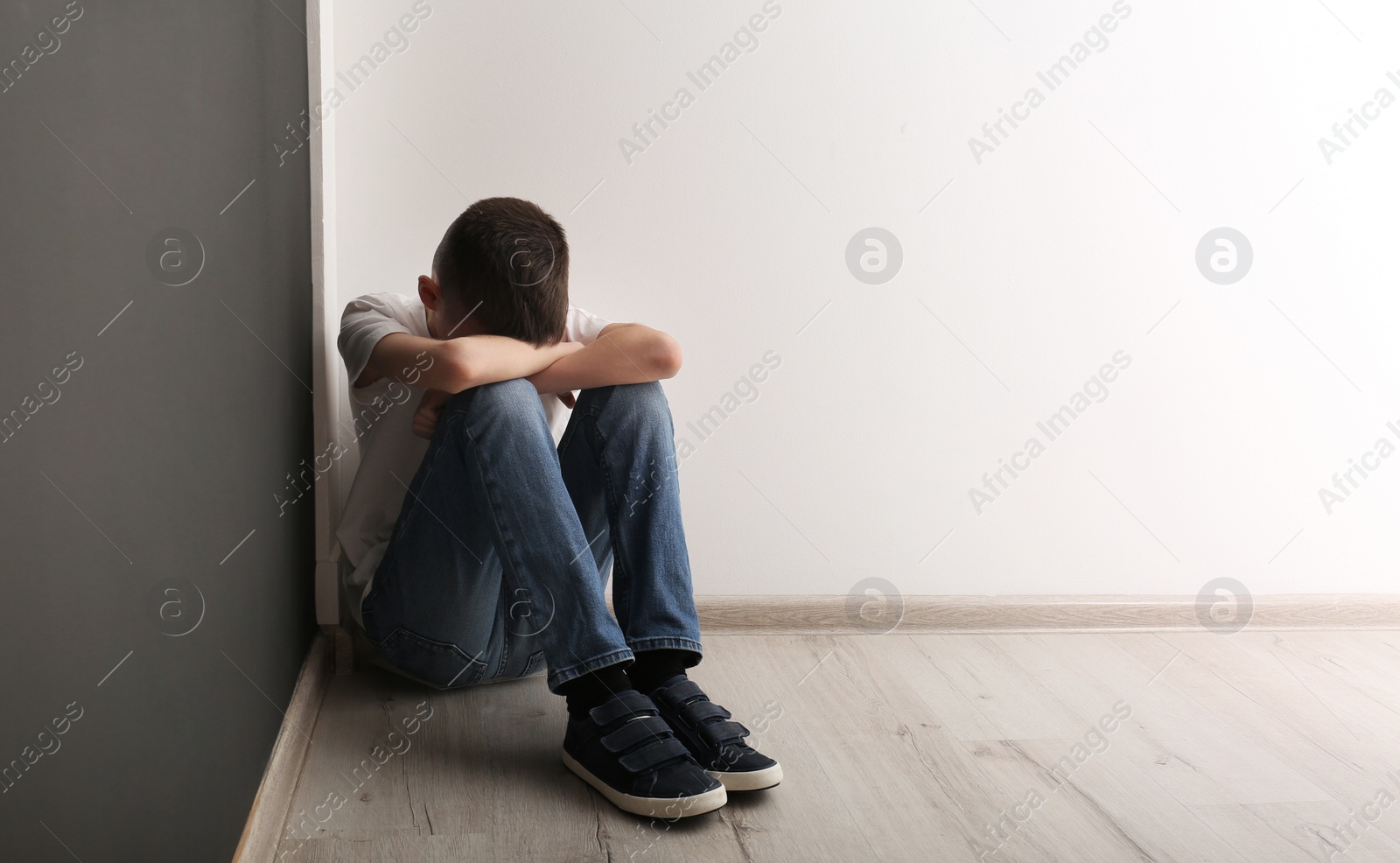 Photo of Upset boy sitting on floor indoors. Space for text