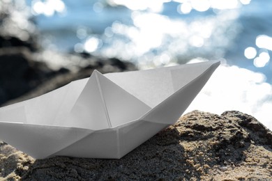 Photo of White paper boat on rock near sea, closeup