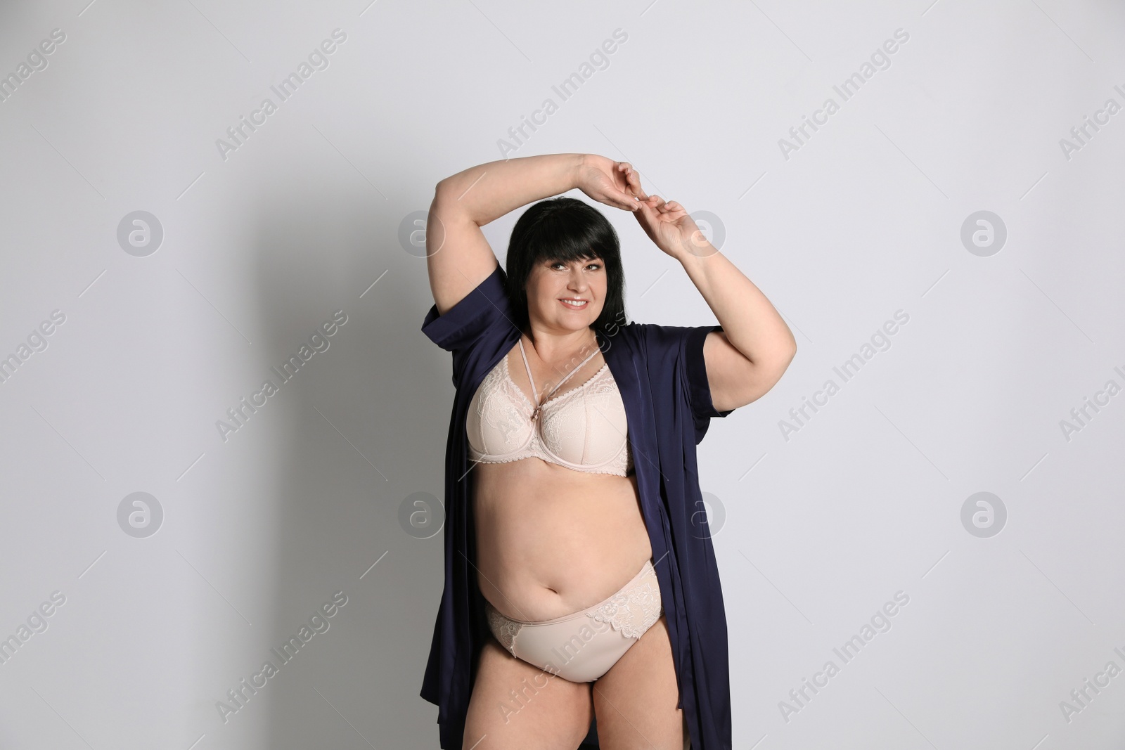 Photo of Beautiful overweight woman in beige underwear and silk robe on light background. Plus-size model