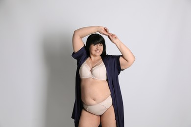 Photo of Beautiful overweight woman in beige underwear and silk robe on light background. Plus-size model