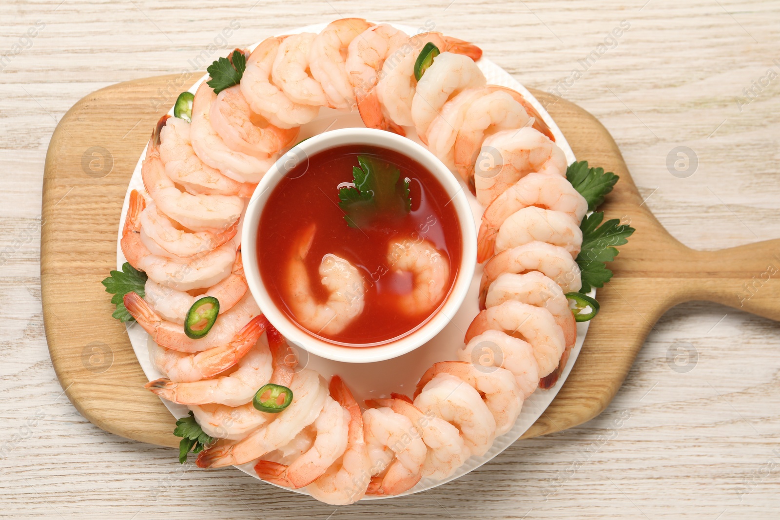 Photo of Tasty boiled shrimps with cocktail sauce, chili and parsley on light wooden table, top view