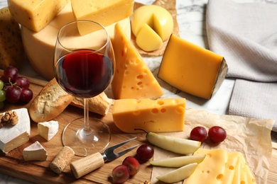 Board with different kinds of delicious cheese, snacks and wine on marble table