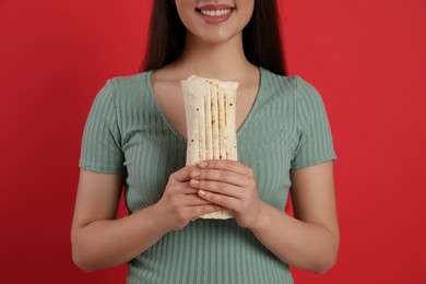 Happy young woman holding tasty shawarma on red background, closeup