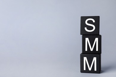 Photo of Black cubes with abbreviation SMM (Social media marketing) on grey background. Space for text