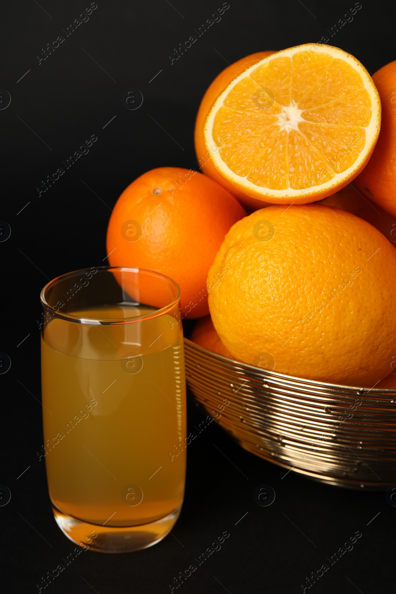 Photo of Bowl with ripe oranges and fresh juice on black background