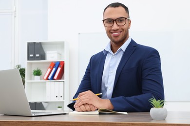 Happy young intern working at table in modern office