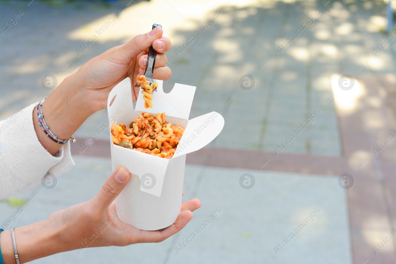 Photo of Woman eating takeaway noodles from paper box with fork outdoors, closeup and space for text. Street food