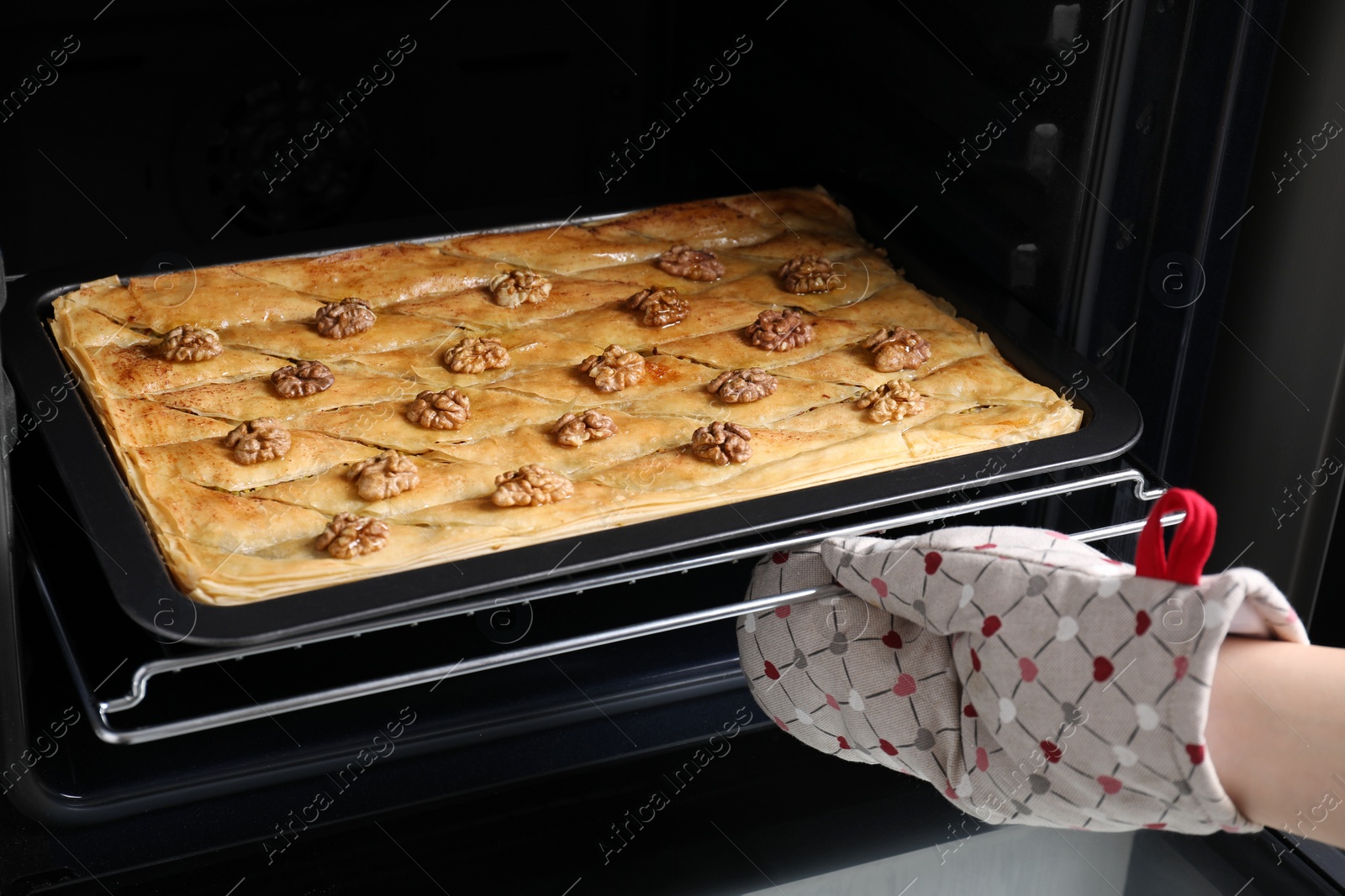Photo of Woman taking out baking pan with delicious baklava from oven, closeup