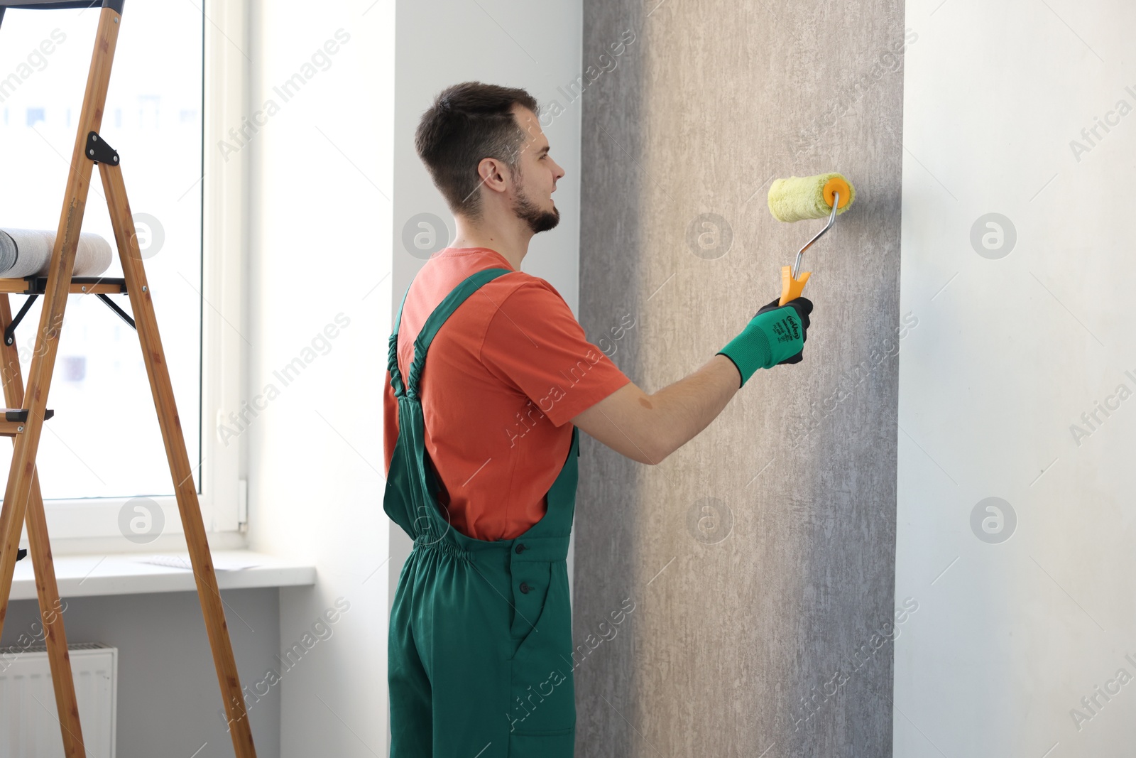 Photo of Man hanging stylish gray wallpaper in room