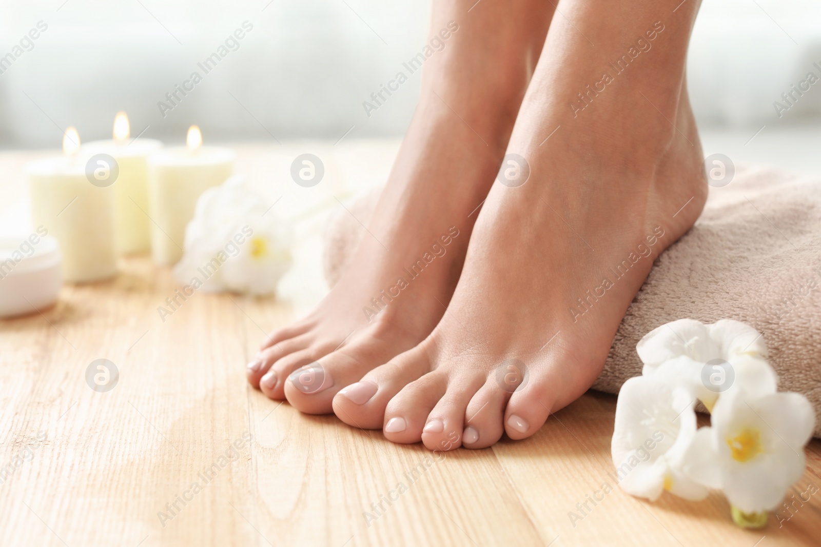 Photo of Woman with beautiful feet, towel and flowers on wooden floor, closeup. Spa treatment