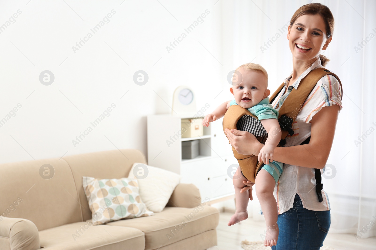 Photo of Woman with her son in baby carrier at home. Space for text