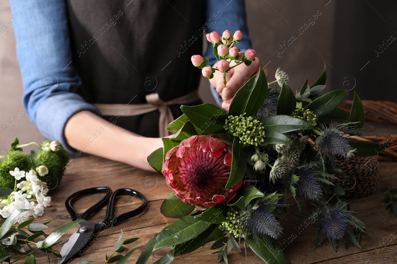 Photo of Florist making beautiful bouquet with fresh flowers at wooden table, closeup