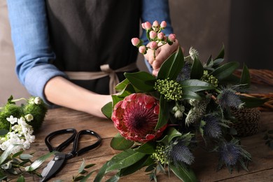 Florist making beautiful bouquet with fresh flowers at wooden table, closeup