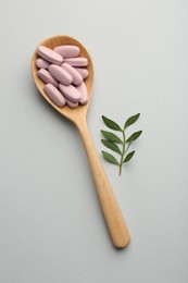 Photo of Vitamin pills in wooden spoon and twig on light grey background, top view. Health supplement