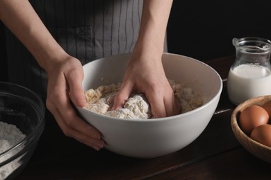 Photo of Making bread. Woman kneading dough at wooden table on dark background, closeup