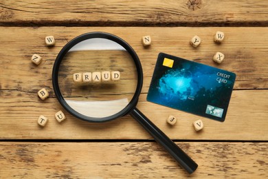 Photo of Word Fraud of cubes with letters, credit card and magnifying glass on wooden background, flat lay