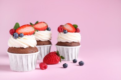 Delicious cupcakes with cream and berries on pink background, space for text
