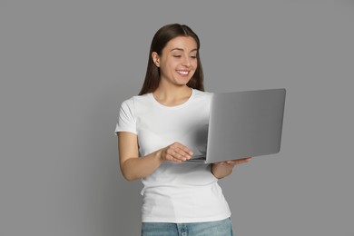 Photo of Young woman with modern laptop on grey background