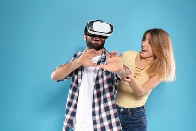 Young man playing video games with VR headset and emotional woman on color background