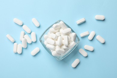 Photo of Vitamin capsules in bowl on light blue background, top view