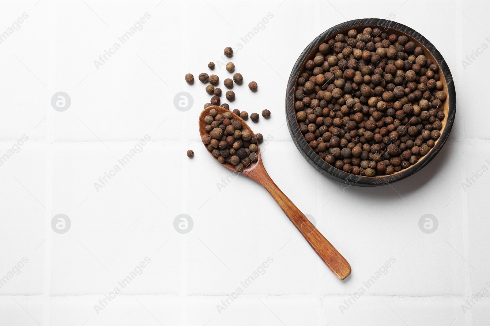Photo of Dry allspice berries (Jamaica pepper) on white tiled table, top view. Space for text