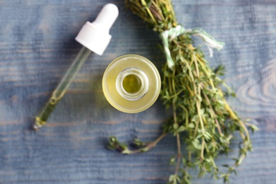 Photo of Bottle of essential oil with thyme on wooden background