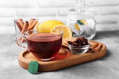 Photo of Tea bag in glass cup, anise stars and cinnamon sticks on light grey table