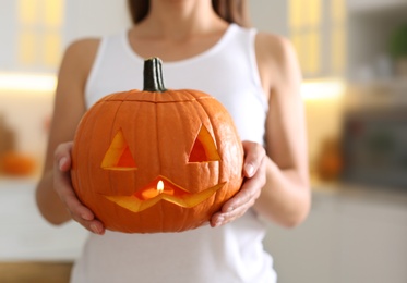 Photo of Woman holding pumpkin jack o'lantern indoors, closeup. Halloween celebration
