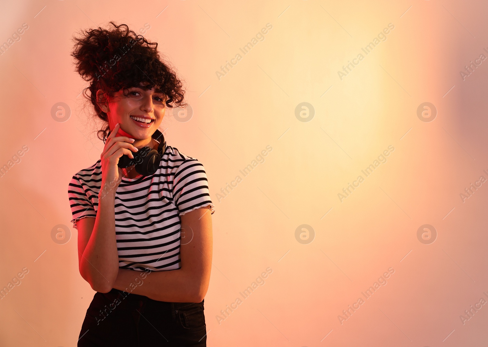 Photo of Beautiful young woman with headphones on color background in neon lights. Space for text