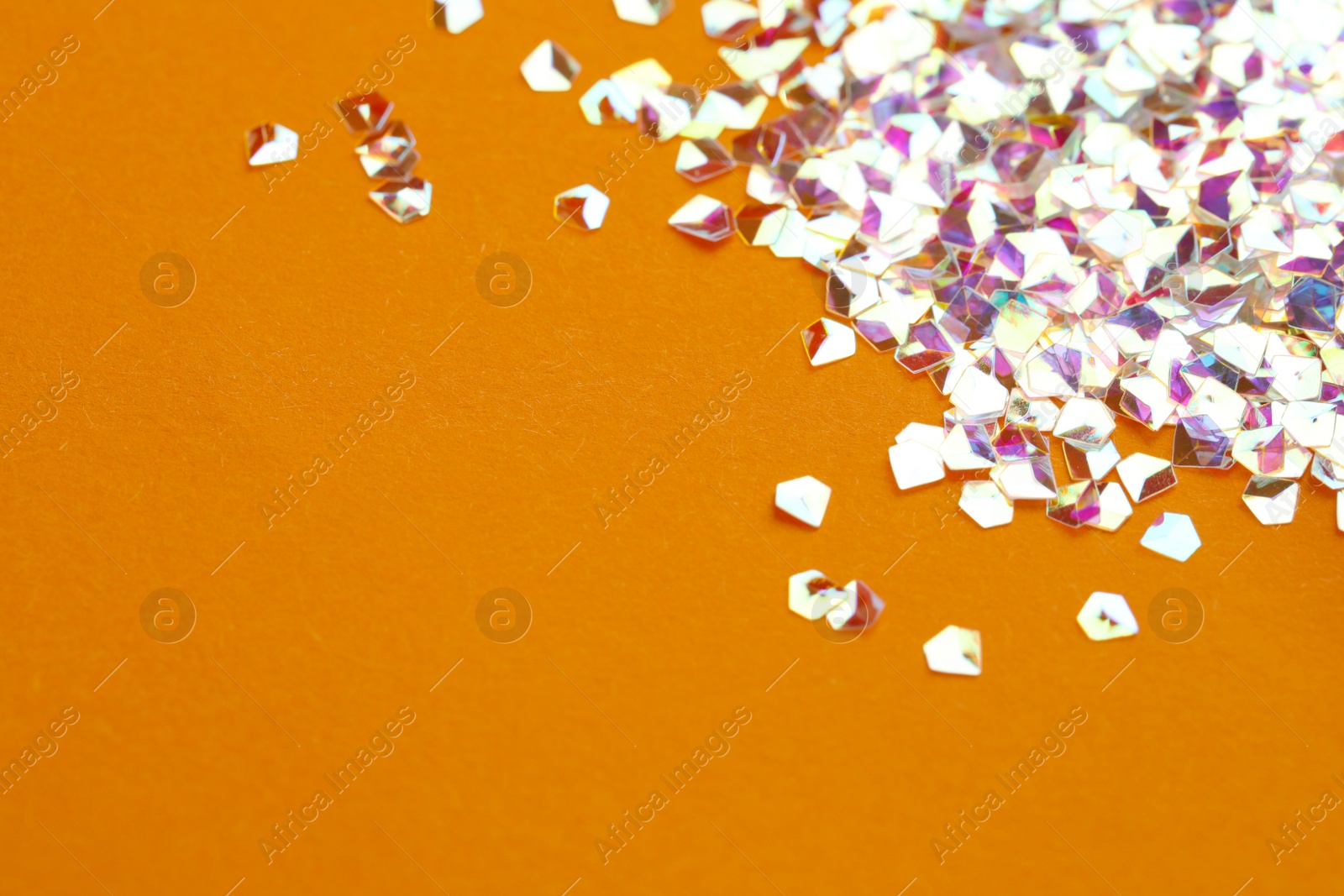 Photo of Pile of shiny glitter on orange background, closeup. Space for text