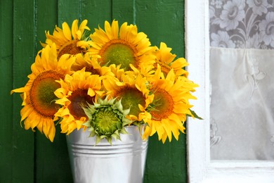 Bouquet of beautiful sunflowers in bucket near window outdoors